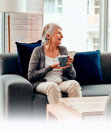 Mujer mayor sentada en un sofá tomando un café.